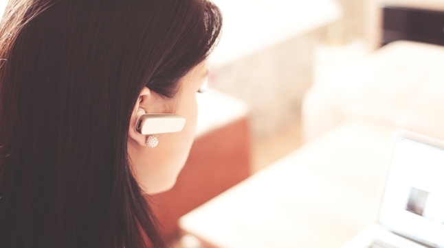 woman with earpiece looking at laptop screen