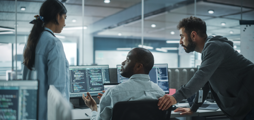 team of three people having a discussion over multiple screens full of data