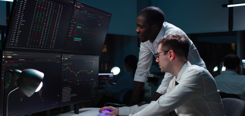 Two people looking at data on four large computer screens