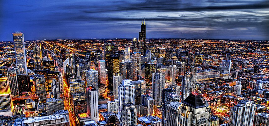 view of lit up city from above, dark clouds in sky