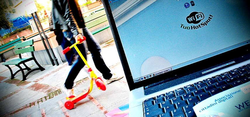 laptop using outdoor hotspot, man with child's scooter in background