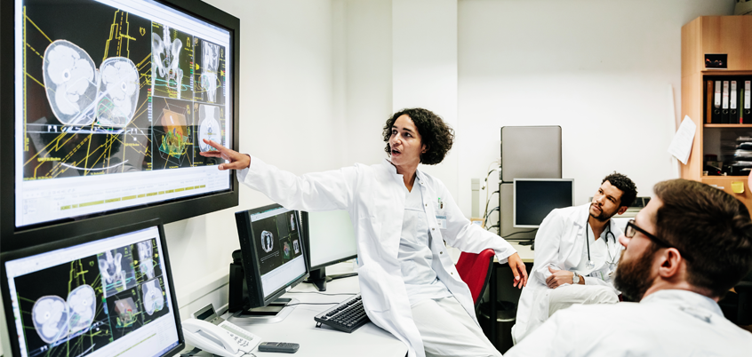 Group of doctors referencing medical imaging on screen.