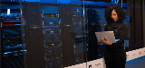 Woman on laptop in front of servers.