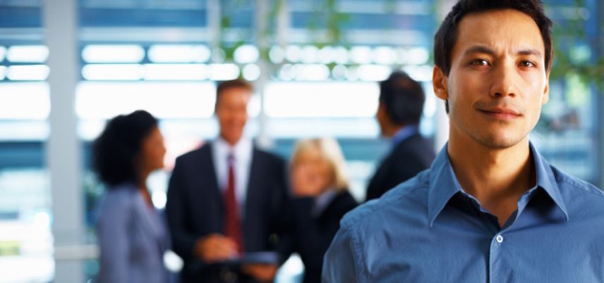 Man in office looking at camera, other people blurred in the background