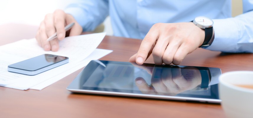 hands of man seated at desk using tablet and smartphone