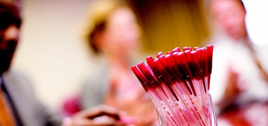 pens in a cup, blurred people in the background