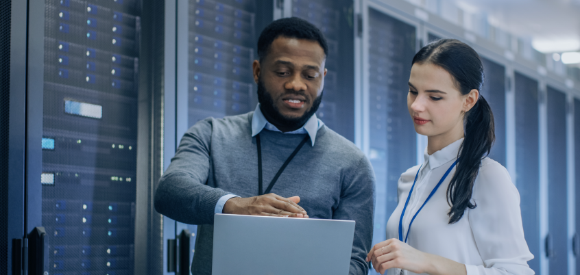 Man and woman standing in front of server looking at laptop