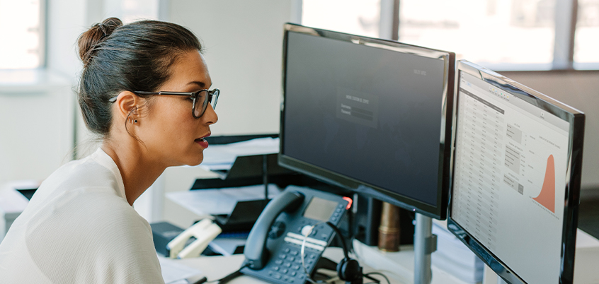 Woman reviewing work on dual monitors