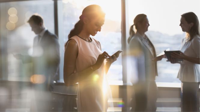 businesswoman looking at phone, people milling about behind her